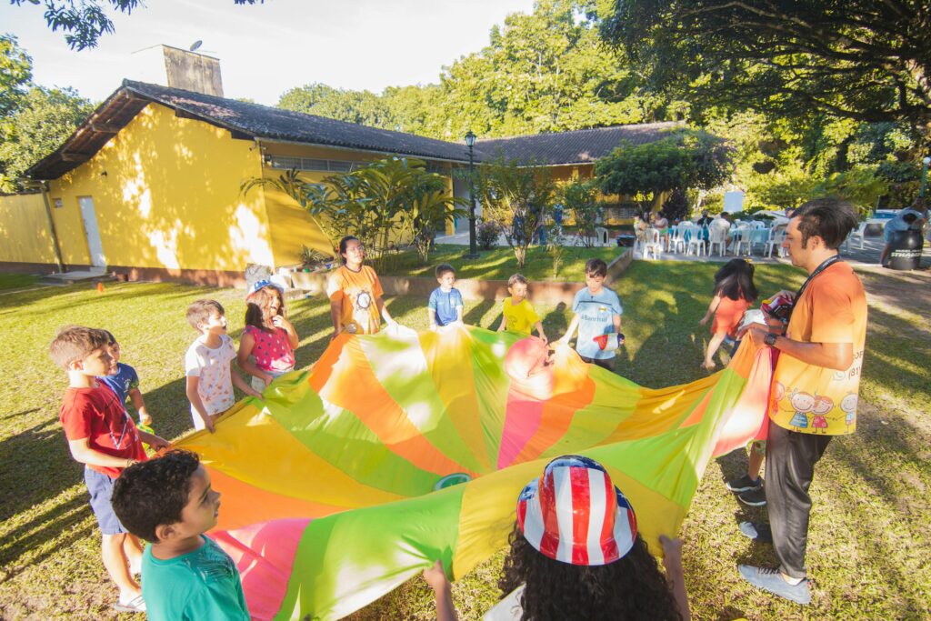 A joyful outdoor birthday party with children playing with a colorful parachute in a garden setting.